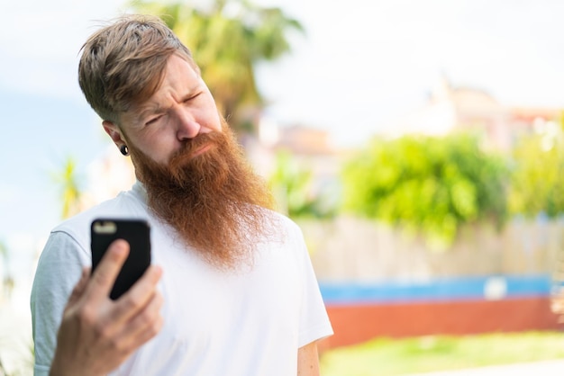 Redhead man with beard using mobile phone at outdoors with sad expression