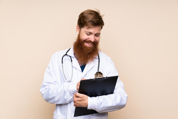 Redhead man with long beard over isolated wall with doctor gown and writing in a folder