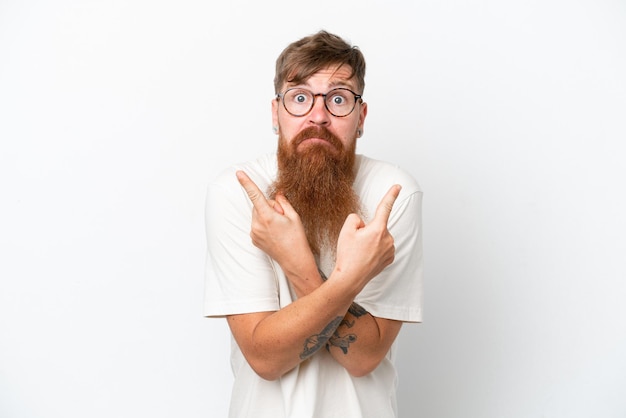 Redhead man with long beard isolated on white background pointing to the laterals having doubts