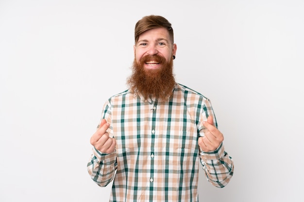 Redhead man with long beard over isolated white wall making money gesture