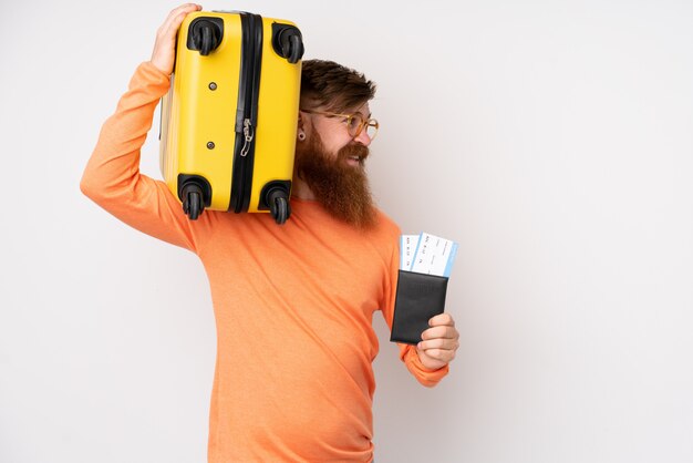 Redhead man with long beard over isolated white wall in vacation with suitcase and passport