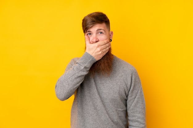 Redhead man with long beard over isolated yellow wall covering mouth with hands