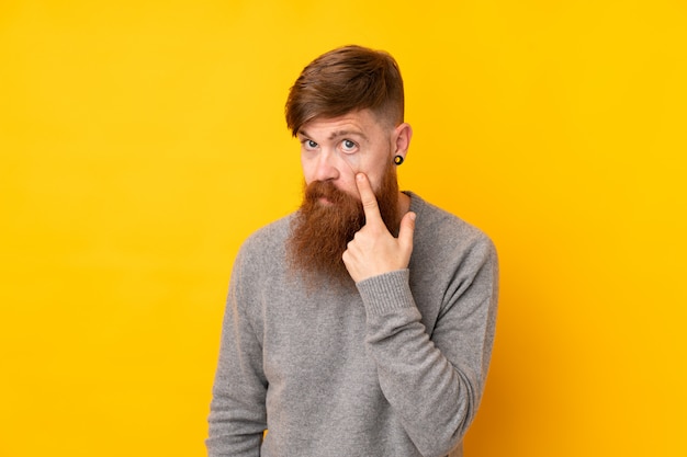 Redhead man with long beard over isolated yellow wall showing something