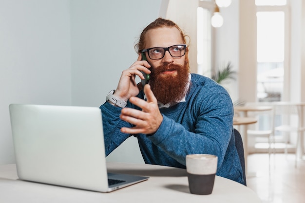 Redhead man working and talking on the phone in a cafe