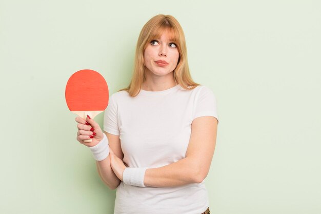 Redhead pretty woman shrugging, feeling confused and uncertain. ping pong concept