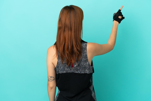 Redhead sport girl isolated on blue background pointing back with the index finger