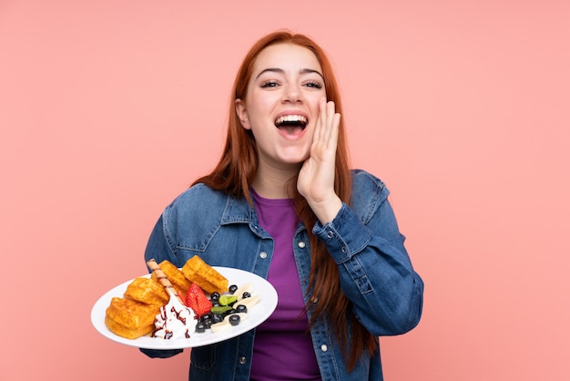 Redhead teenager woman holding waffles shouting with mouth wide open