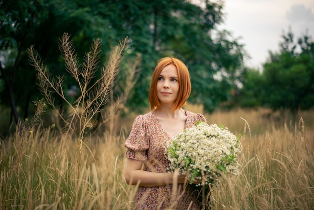 Redhead woman of forty years with a large bouquet of wildflowers in summer in nature