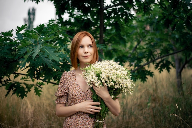 Redhead woman of forty years with a large bouquet of wildflowers in summer in nature