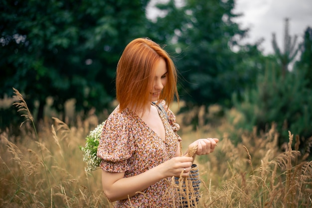 Redhead woman of forty years with a large bouquet of wildflowers in summer in nature