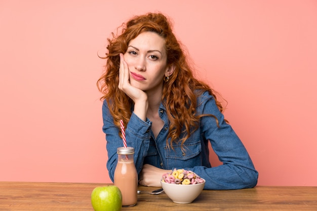 Photo redhead woman having breakfast cereals and fruit unhappy and frustrated