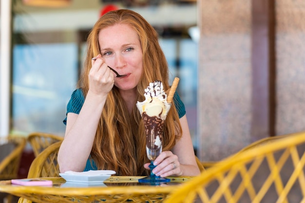 Photo redhead woman having a glass of ice cream on a terrace of an ice cream parlor