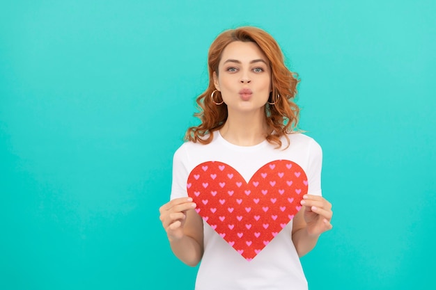 Redhead woman hold red heart on blue background kiss