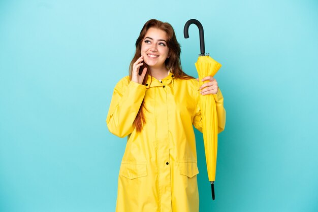 Redhead woman holding an umbrella isolated on blue background thinking an idea while looking up