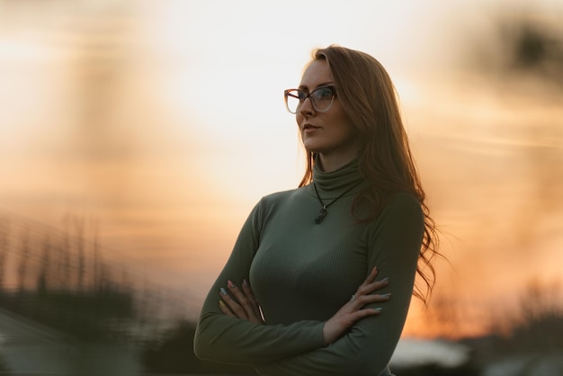 A redhead woman is posing in the background of the cloudy evening sky