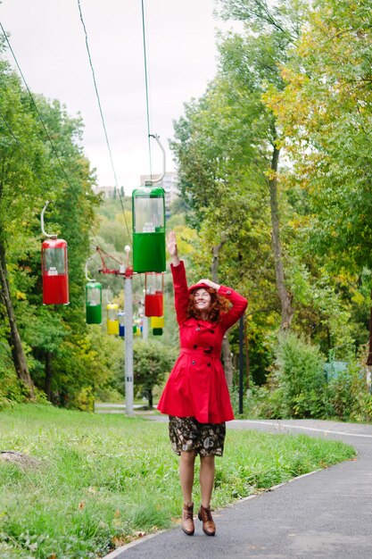 Redhead woman in a red beret, coat walking in autumn park, smiling, enjoying life. cable car. fall