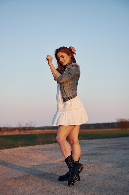 Redhead woman in skirt standing and posing for a camera on the road at evening time