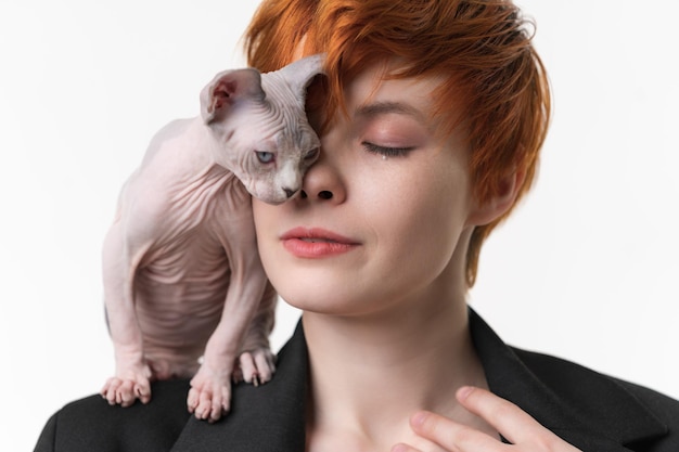 Redhead woman with closed eyes and playful kitten stands on her shoulder gently pressed against face