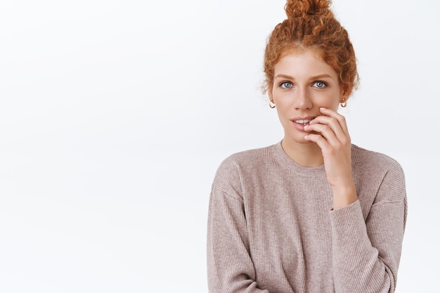 redhead woman with curly hair with combed hair in bun, touching lip and looking at front intrigued