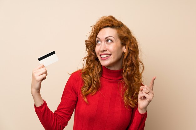 Redhead woman with turtleneck sweater holding a credit card