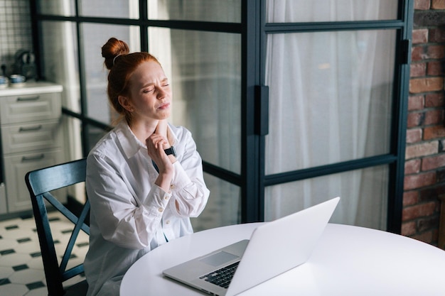 Redhead young business woman having wrist pain during working at laptop while sitting at desk