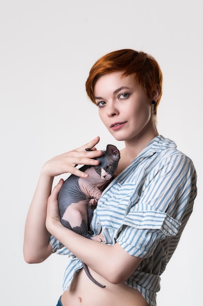 Redhead young woman gently hugging Sphynx Cat looking at camera Studio shot on white background