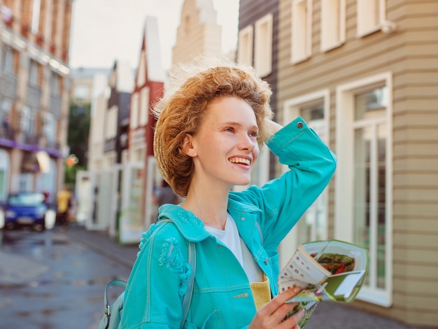 redhead young woman in straw hat and with travel bag with paper map travel over west europe