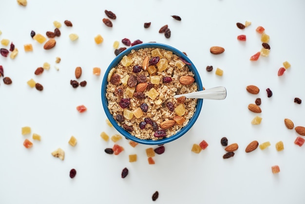 Reduce callories. Top view of healthy and useful breakfast, oats in bowl and dry fruits isolated on white background. Healthy snack or breakfast in the morning. Metal spoon in muesli