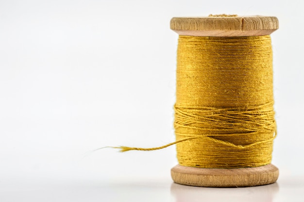 Reel or spool of yellow sewing thread isolated on white. Shallow depth of field. Close-up macro shot.