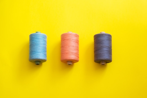 Reels with threads of different colors and sizes on a bright, colorful background. Flat lay