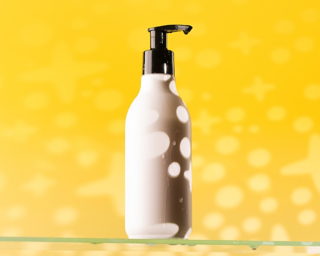 Refillable white dispenser bottle with a cosmetic product on a glass shelf on a yellow background with a shadow pattern