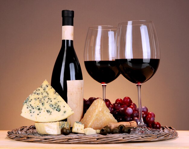 Refined still life of wine cheese and grapes on wicker tray on wooden table on beige background