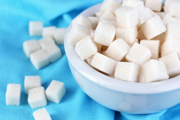 Refined sugar in bowl on color fabric background