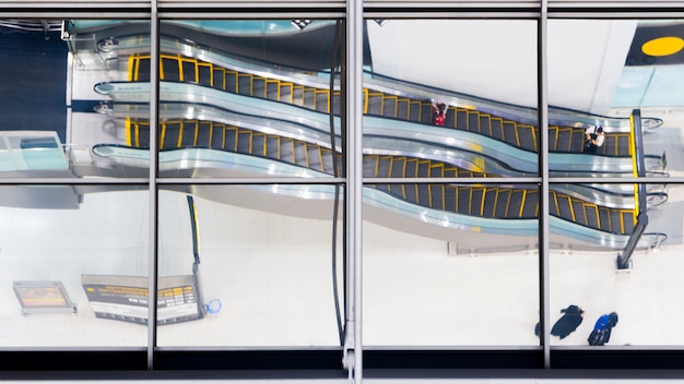 Reflection glass of top view people walk and sit stair escalator at airport.