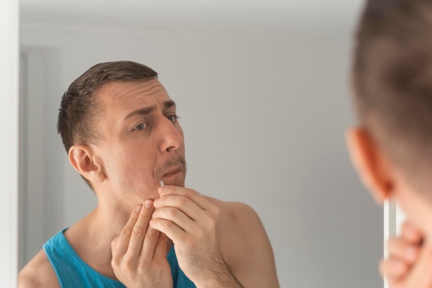 Reflection of man in mirror removing hair above upper lip Morning routine in bathroom View from behind the shoulder