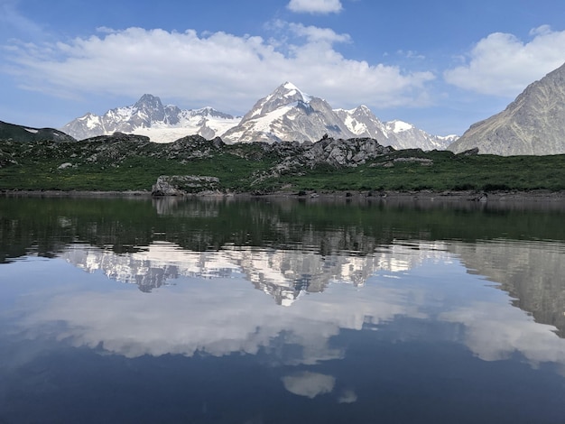 Reflection of mountains and sky in the pond, in the Italian Alps. Aosta Valley with snow covered mountains in the background and grassland near the water.