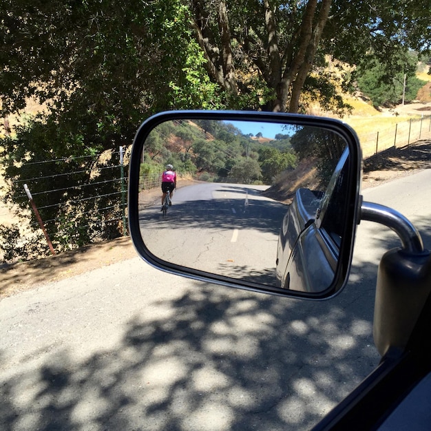 Reflection of woman in car mirror while riding bicycle