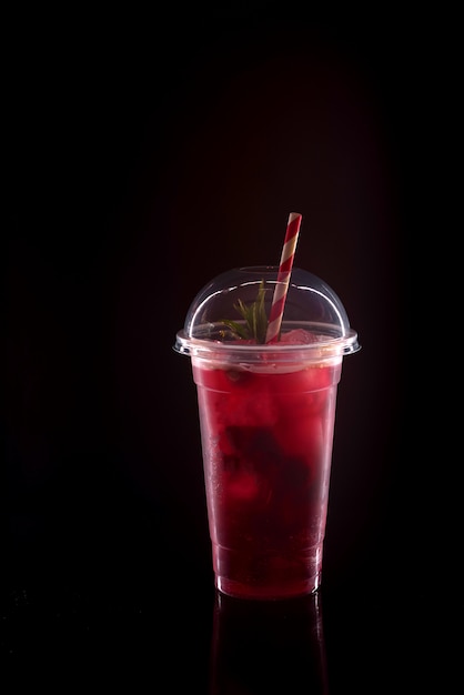 Refreshing cool lemonade with strawberries, mint and ice in plastic glass with lid on black background