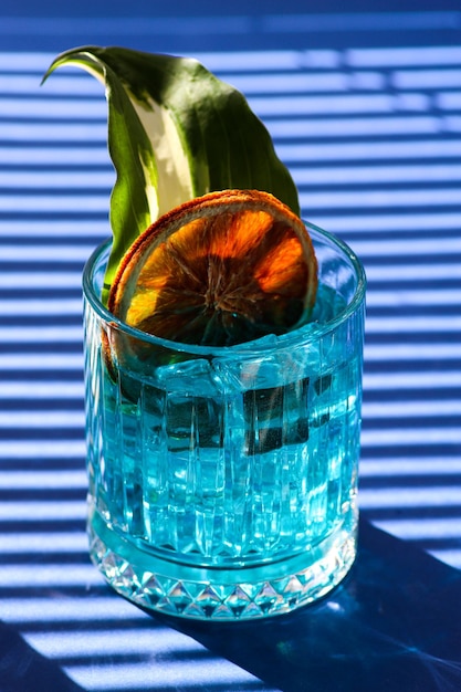 Refreshing and cooling blue cocktail with ice cubes and a slice of dried orange and green leaf