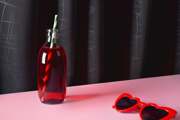 Refreshing cranberrie lemonade cocktail in bottle with palm leaf on pink table