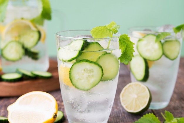 Refreshing detox water with cucumber, lemon and fresh mint on a light green background. Organic, vegan beverage.