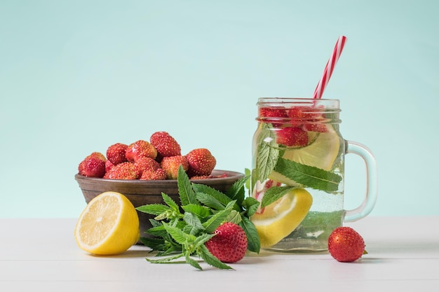 A refreshing drink of berries lemon and mint and a bowl of strawberries on a white table