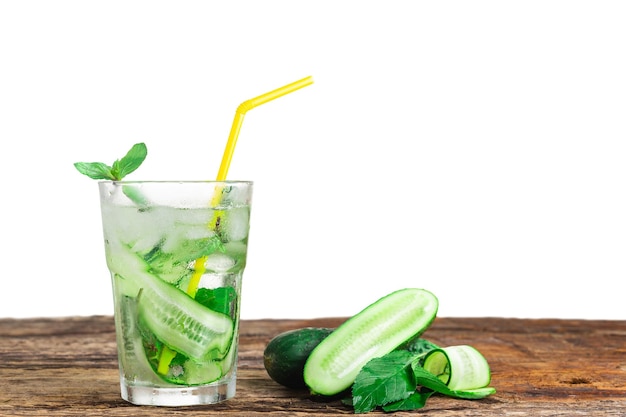 Refreshing drink with cucumber and mint in a glass with a straw next to ice cubes against a green ba