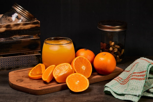 Refreshing glass with fresh orange juice, ice and oranges on a wooden table in dark background