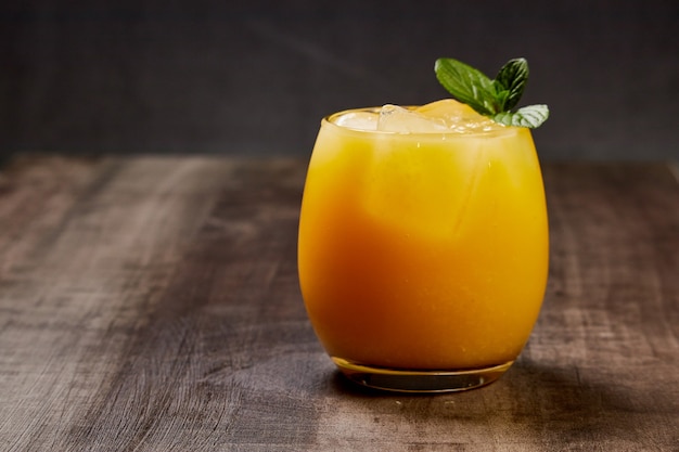 Refreshing glass with orange juice, ice and mint on a wooden table in dark background