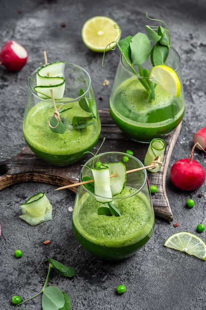 Refreshing kale cucumber green smoothie in a glass on concrete background Detox smoothie green fresh peas cucumber radish spinach and lime vertical image top view