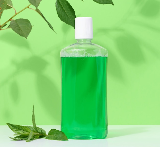 Refreshing mouthwash in a transparent plastic bottle on a green background