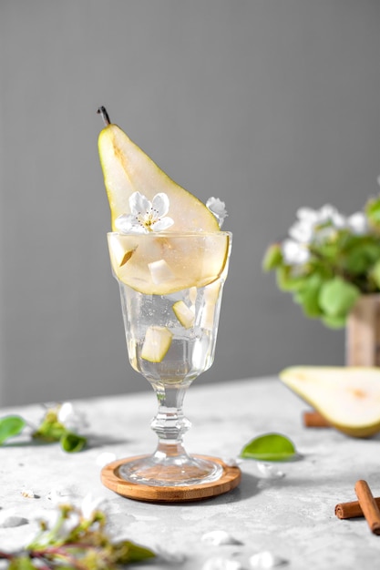 Refreshing Pear cocktail in a glass decorated with fresh fruit and flowers on light gray background Summer mocktail