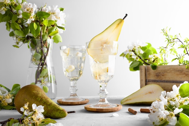 Refreshing Pear cocktail lemonade in a glasse with pear puree and fresh fruit and flowers on light gray table background