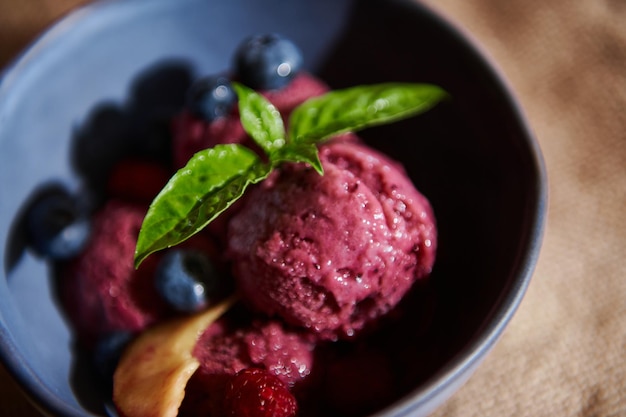 Refreshing raw vegan purple berry sorbet on navy ceramic bowl with lemon basil leaves blueberries and juicy peaches